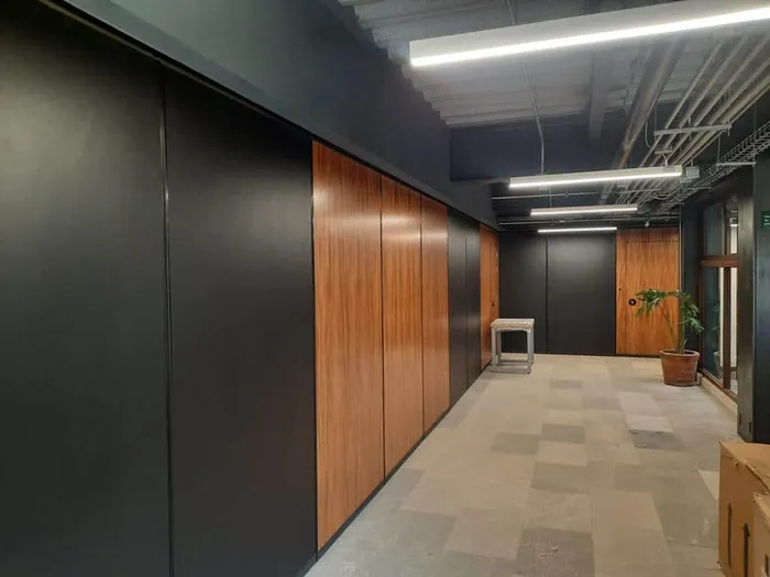 Pasillo corporativo con muros divisorios en acabado negro y chapa de madera