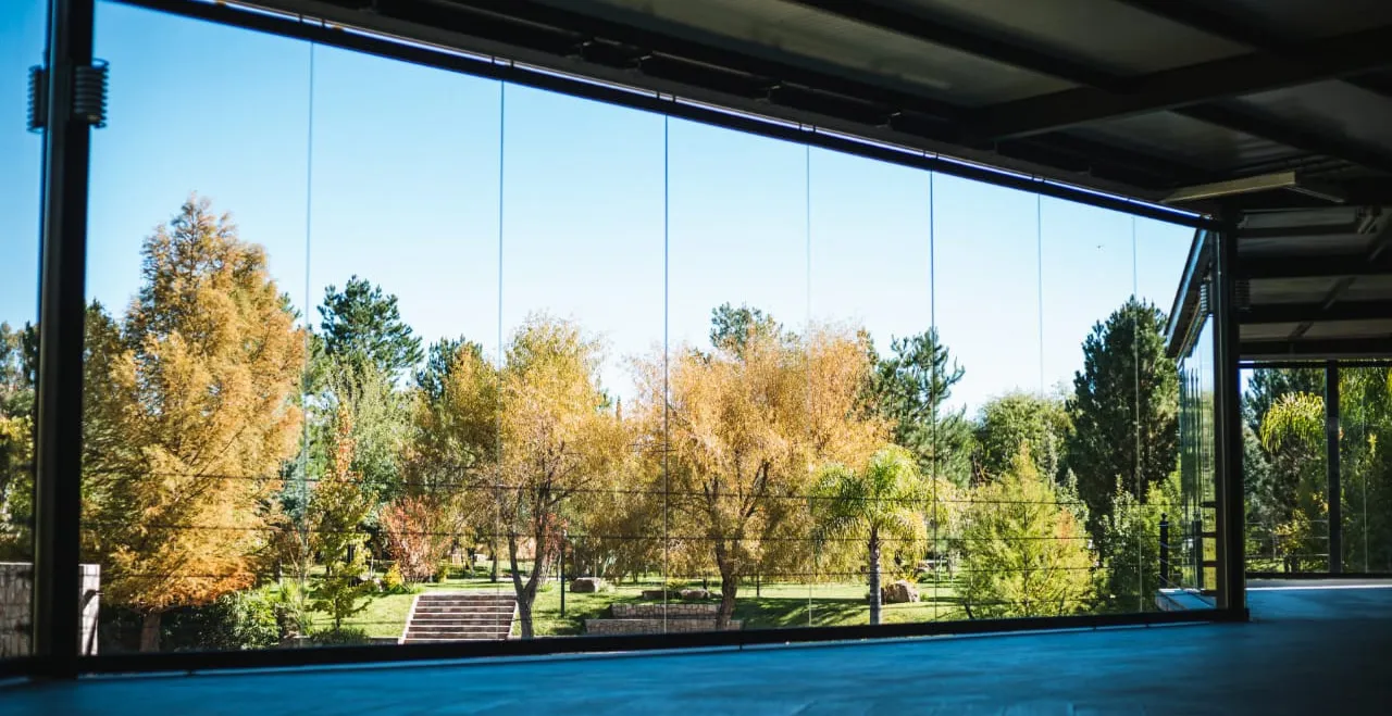 Muro móvil de cristal abierto hacia un jardín arbolado, instalación real Zurbía